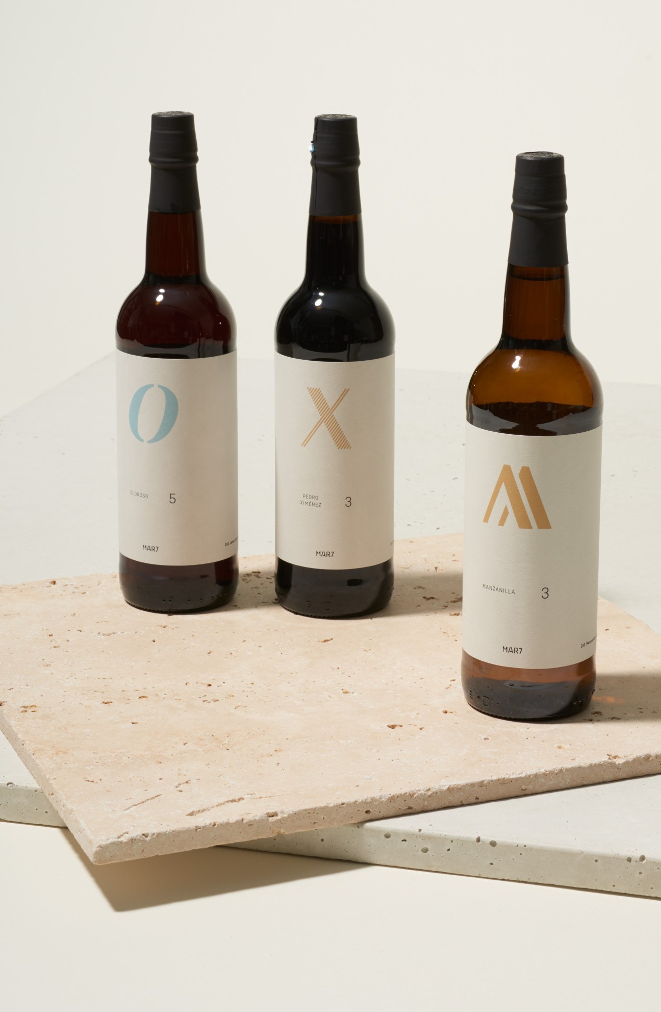 Three bottles of Mar7 sherry with minimalist label designs featuring geometric symbols on a stone surface.