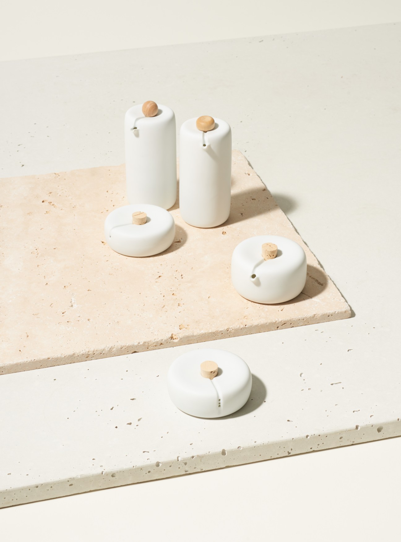 Kanz Architetti Bombette dressing set with white porcelain vessels and wooden tops on travertine surface.