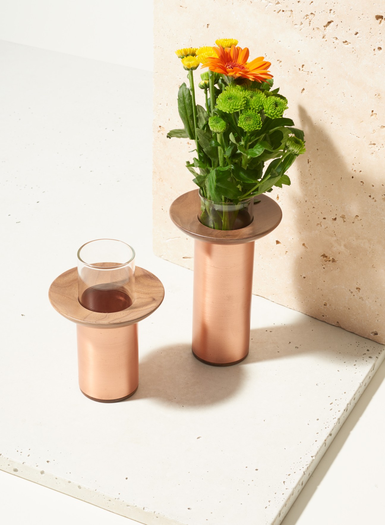 Two Nir Meiri vases with copper bases, wooden sepal trays, and glass vessels displaying fresh flowers.