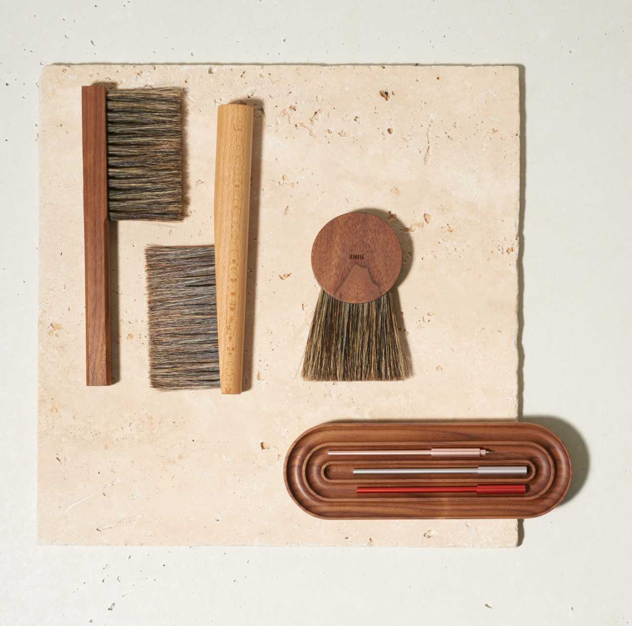 Collection of handmade brushes and pens by Hine and Ensso with wooden handles arranged on a textured surface.
