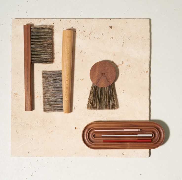 Flat lay of Hine brushes and Ensso pens on a textured cream background, including wooden-handled brushes and a wooden pen holder.