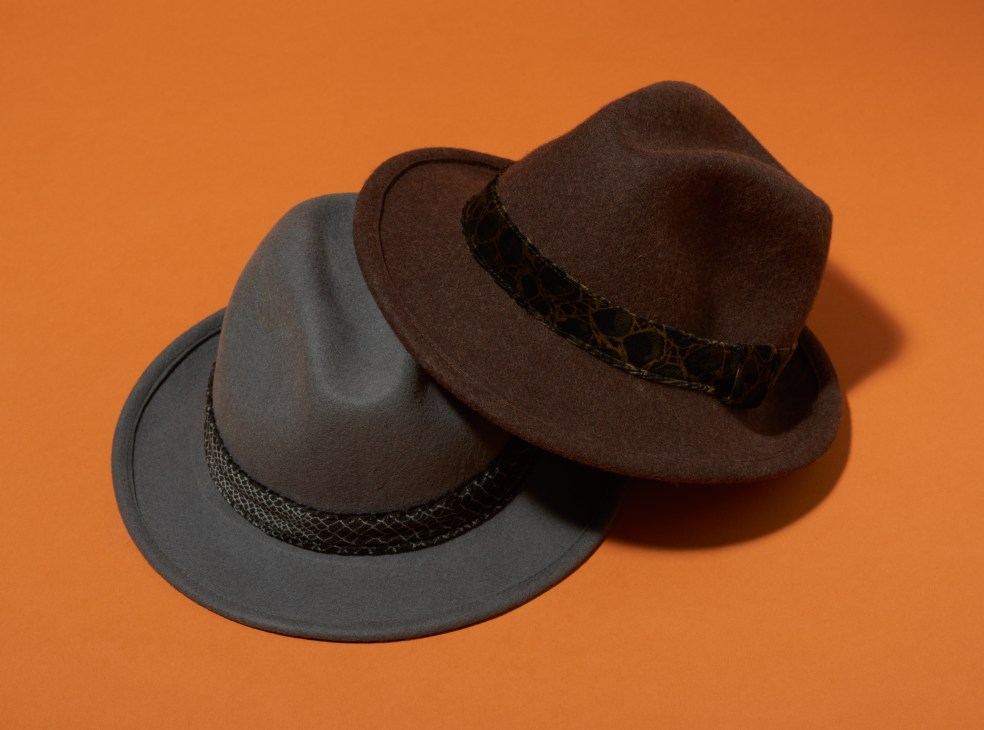 Two felt hats with braided leather bands against an orange background