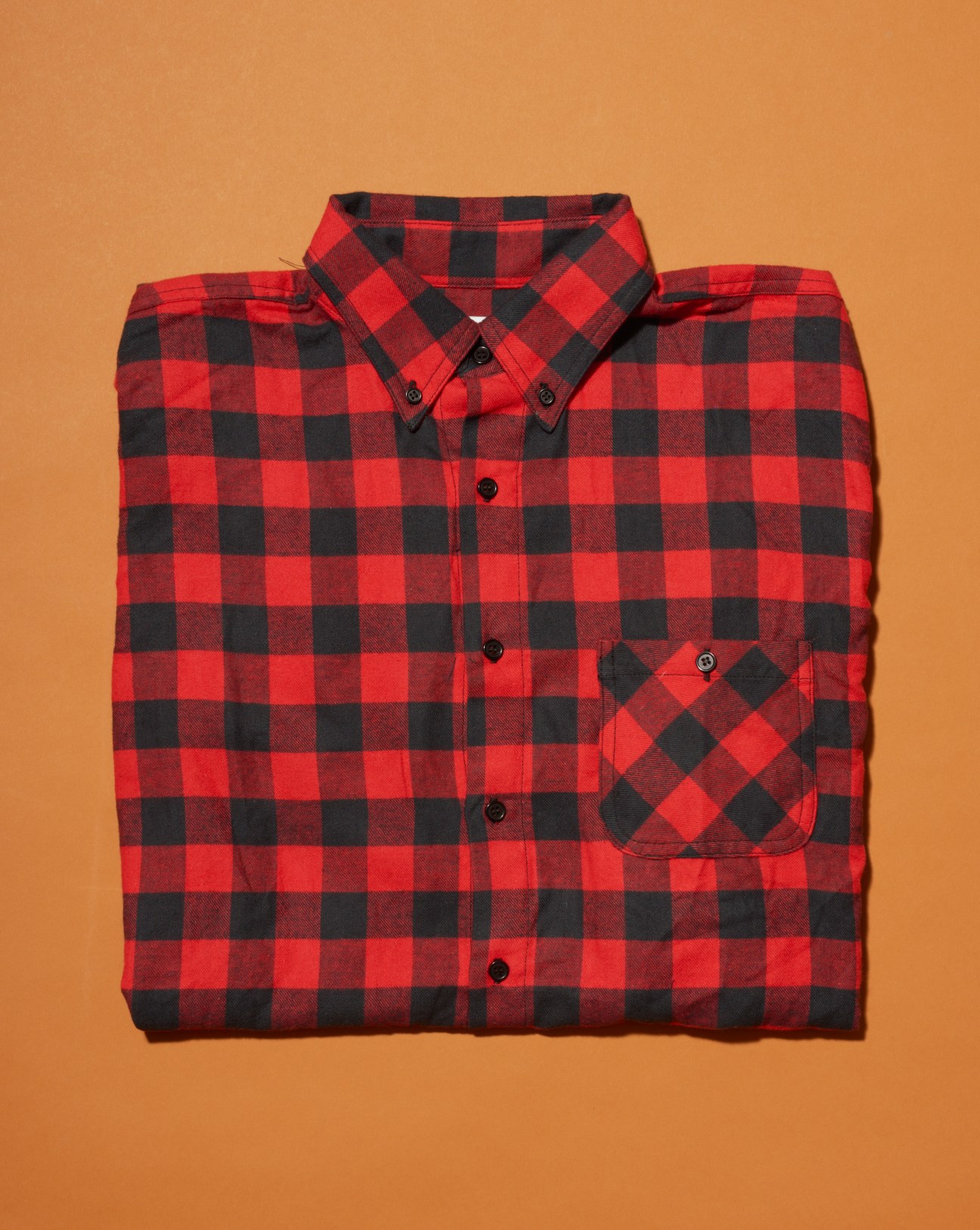 Red and black checkered flannel shirt folded on orange background