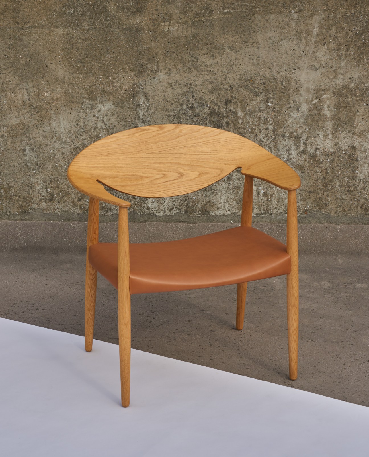 Carl Hansen Metropolitan chair with cognac leather seat and curved oak frame against concrete wall