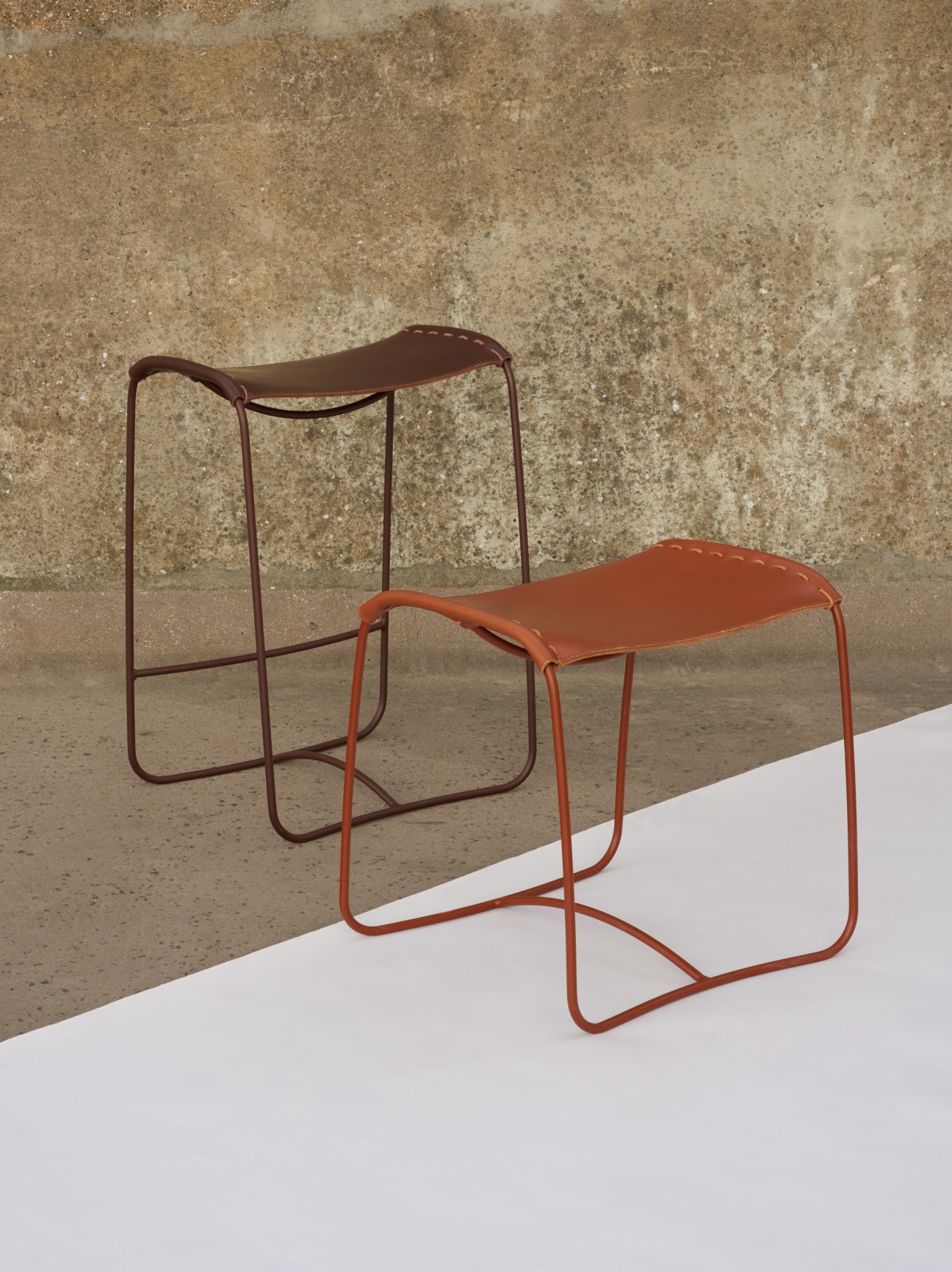 Two modern stackable stools with curved leather seats and powder-coated steel frames in orange and burgundy