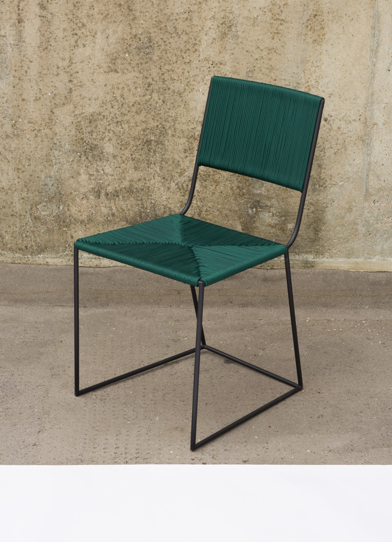 Green woven cord seat chair with black metal frame against concrete wall