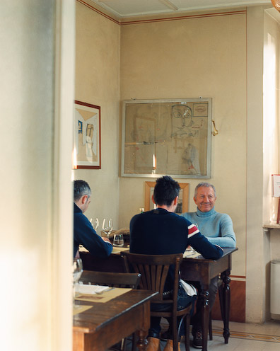 Three men dining at a wooden table in a warm, traditionally decorated Italian restaurant interior.