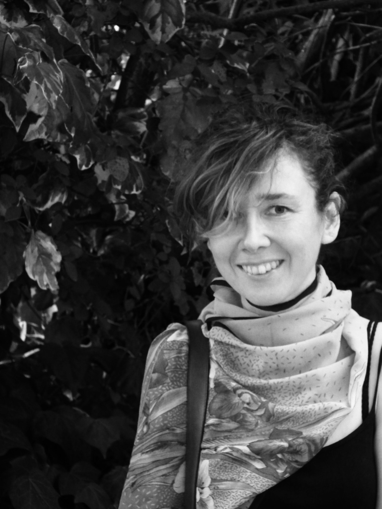 Black and white portrait of Ivana Katuric, urban planner, smiling outdoors with foliage behind her.