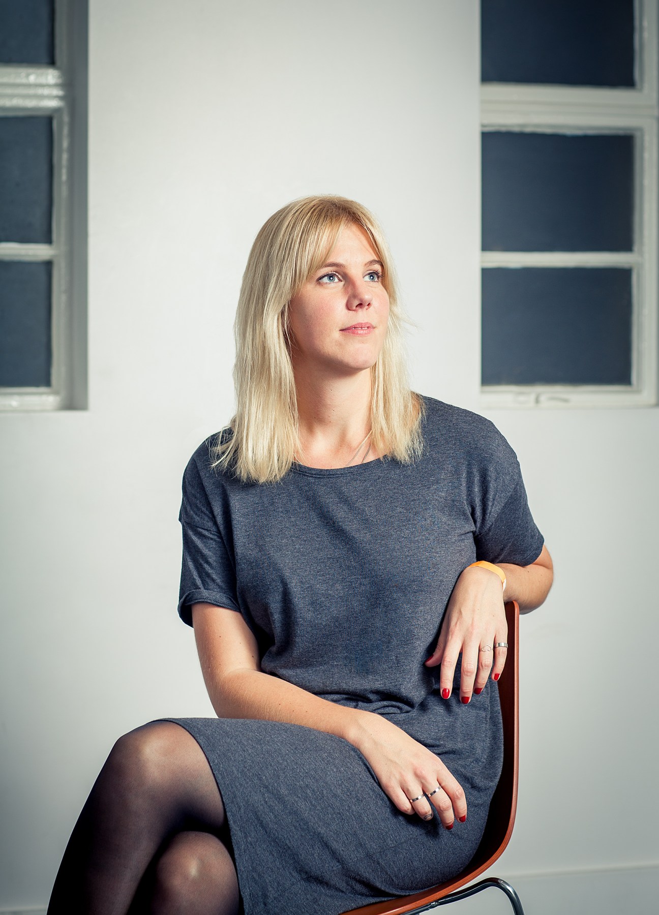 Nina Finnerud, project manager of Ja Ja Ja Festival, sits on a wooden chair against a white wall with windows.