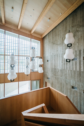 Interior of Swiss embassy in Seoul featuring white pendant lights, wooden ceiling beams, and concrete walls.