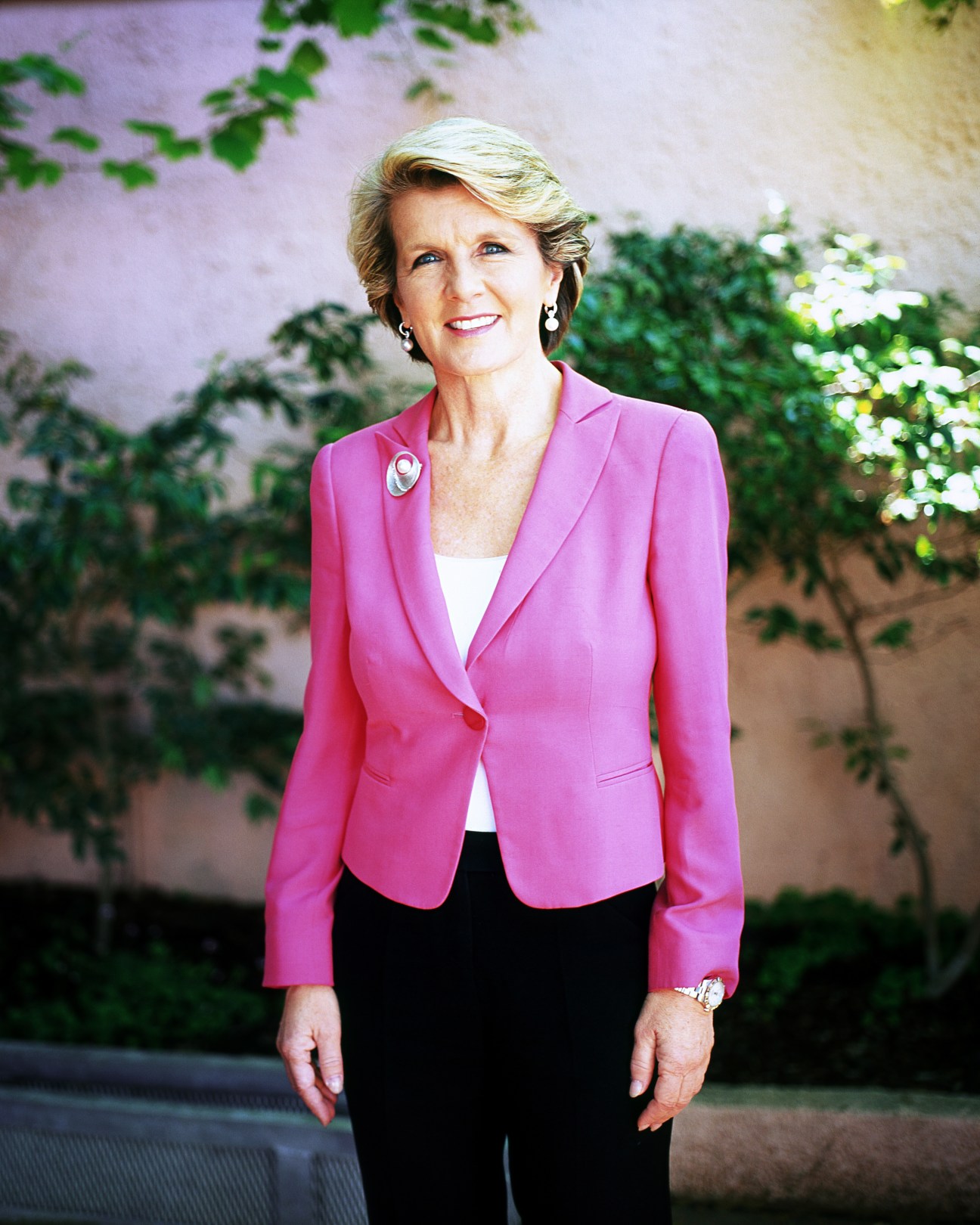 Julie Bishop, Australia's foreign minister, wearing a bright pink blazer and standing against a garden wall backdrop.