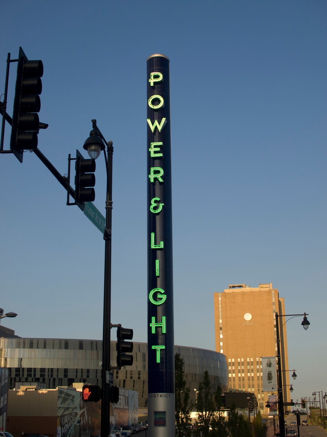 A neon sign reading "Power & Light" with traffic lights and downtown buildings against blue sky.