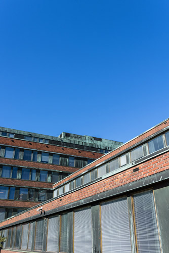 Exterior view of the National Pensions Institute building designed by Alvar Aalto, showing distinctive angular brick architecture against a clear blue sky.