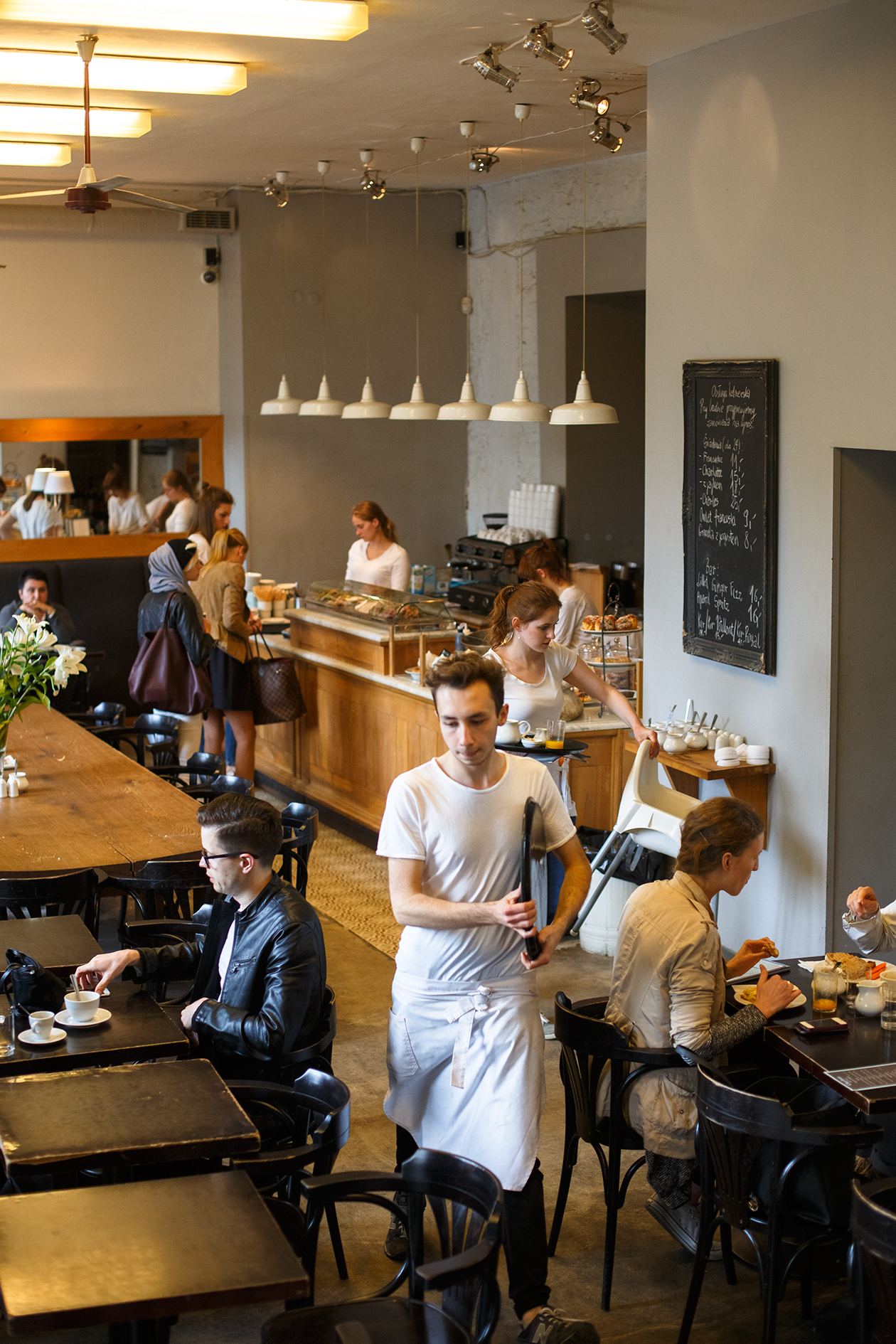 Interior of Top Paddock café in Melbourne showing staff and customers in a spacious venue with wooden tables and pendant lighting.