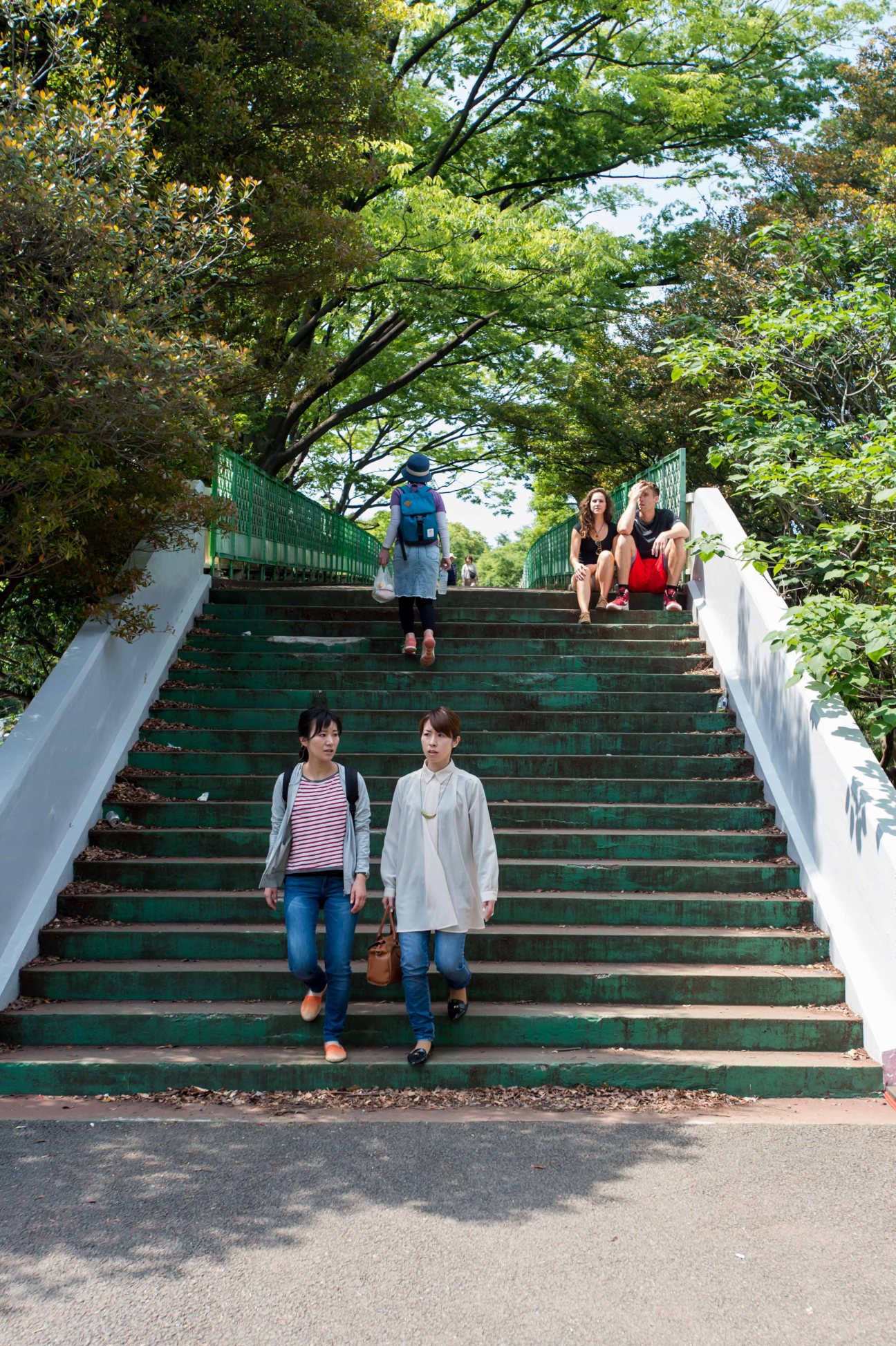 People walking on tree-lined green stairs in an urban park setting.