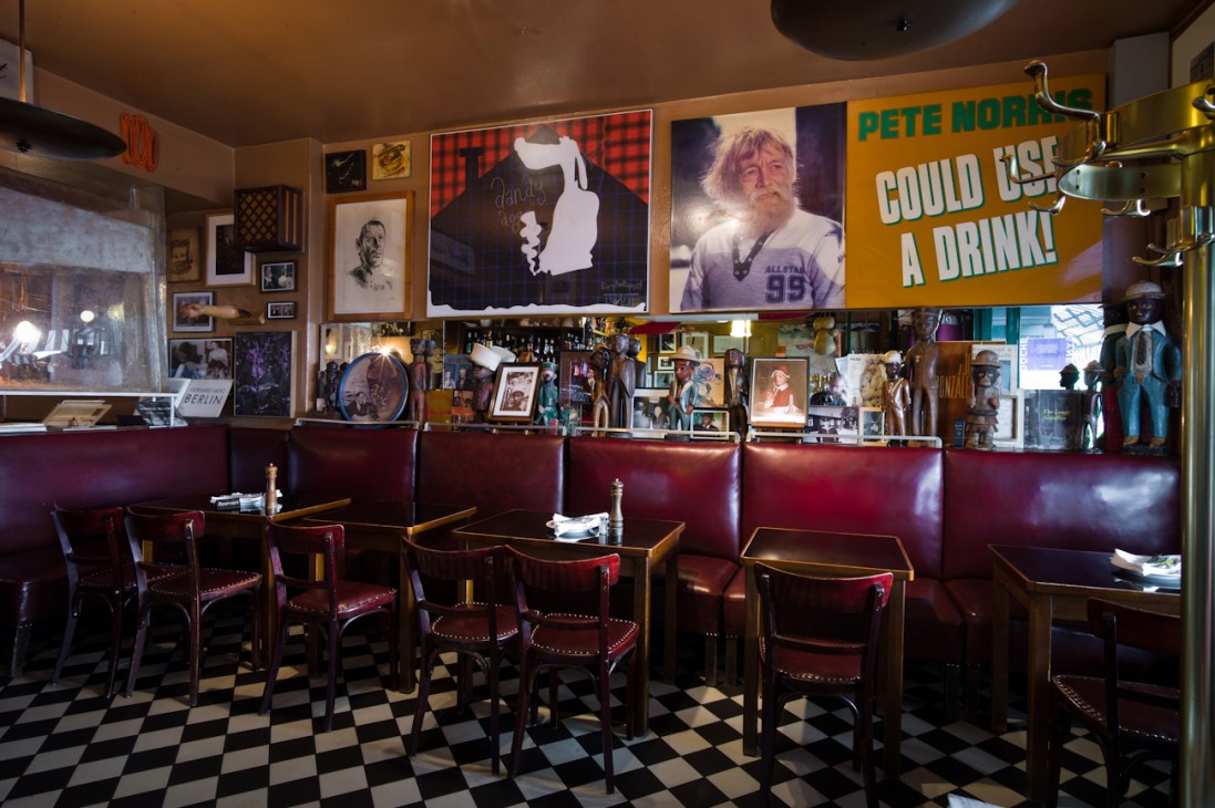 Interior of Paris Bar in Berlin showing red leather banquettes, small tables, and walls covered with eclectic artwork and vintage memorabilia.