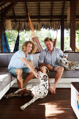 Two people sit on a sofa with a dalmatian dog in a rustic wooden cabin interior.