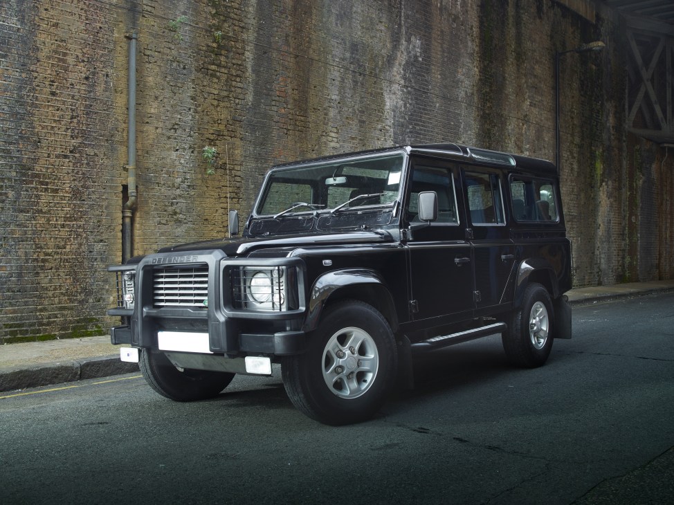 Black Land Rover Defender parked against a weathered brick wall.