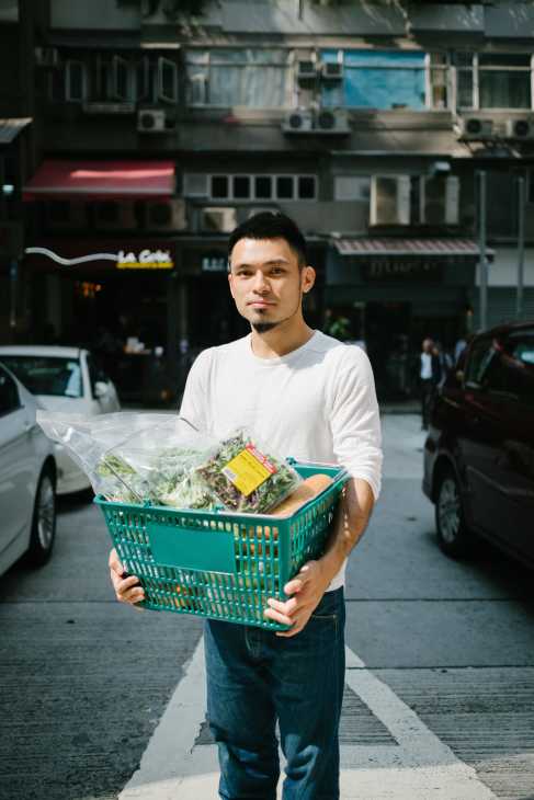 Man holding a turquoise basket of fresh groceries on a Hong Kong street.