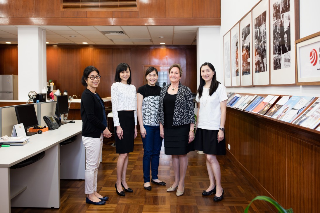 Five women staff members pose together in the modern wood-paneled office of the Asia Global Institute in Hong Kong.
