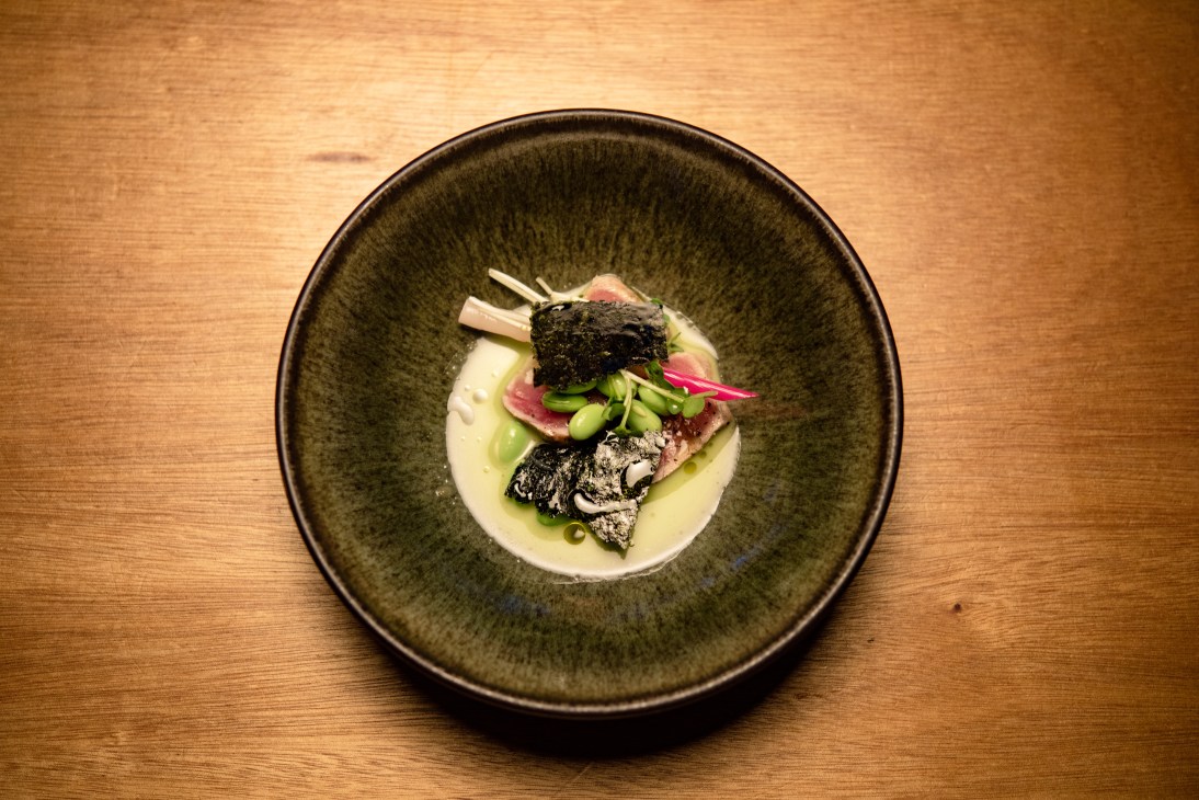 Tuna tataki dish with shishito pepper, edamame, and nori seaweed in a dark ceramic bowl.