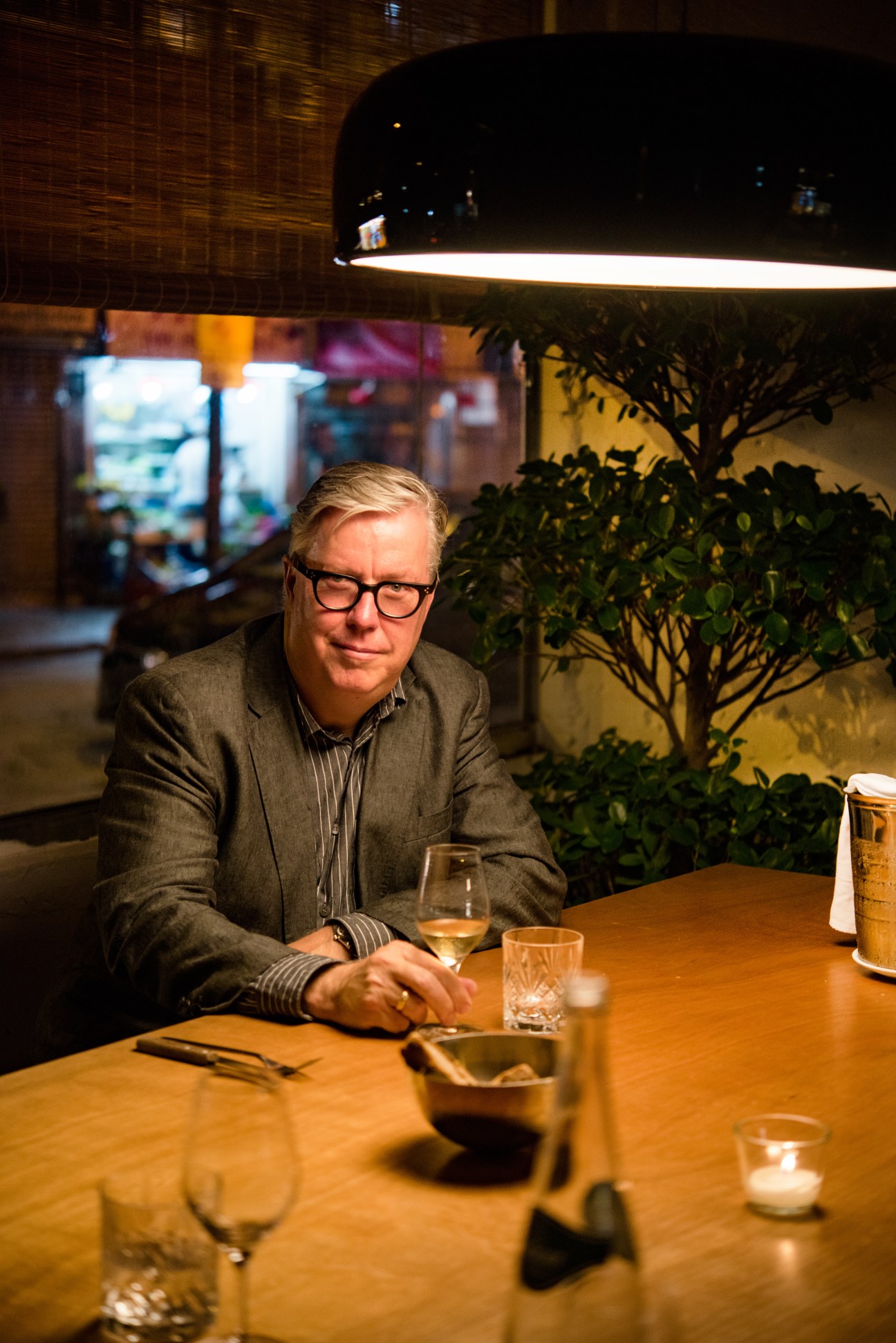 Lars Nittve seated at a dining table at Serge et Le Phoque restaurant with Wan Chai market visible through the window behind him.
