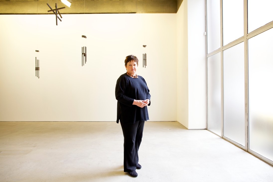 Luisa Strina stands in a gallery space with minimalist artworks displayed on cream-colored walls.