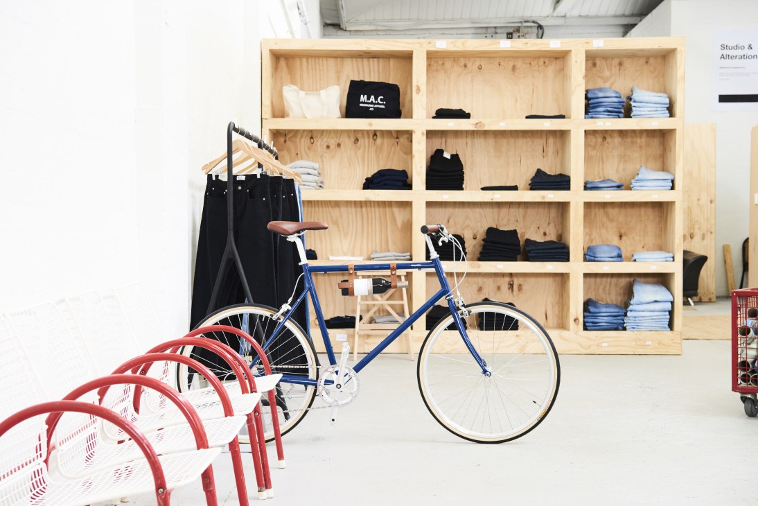 Melbourne Apparel Company shop interior with wooden shelving displaying folded clothes, a blue bicycle, and red bike racks.