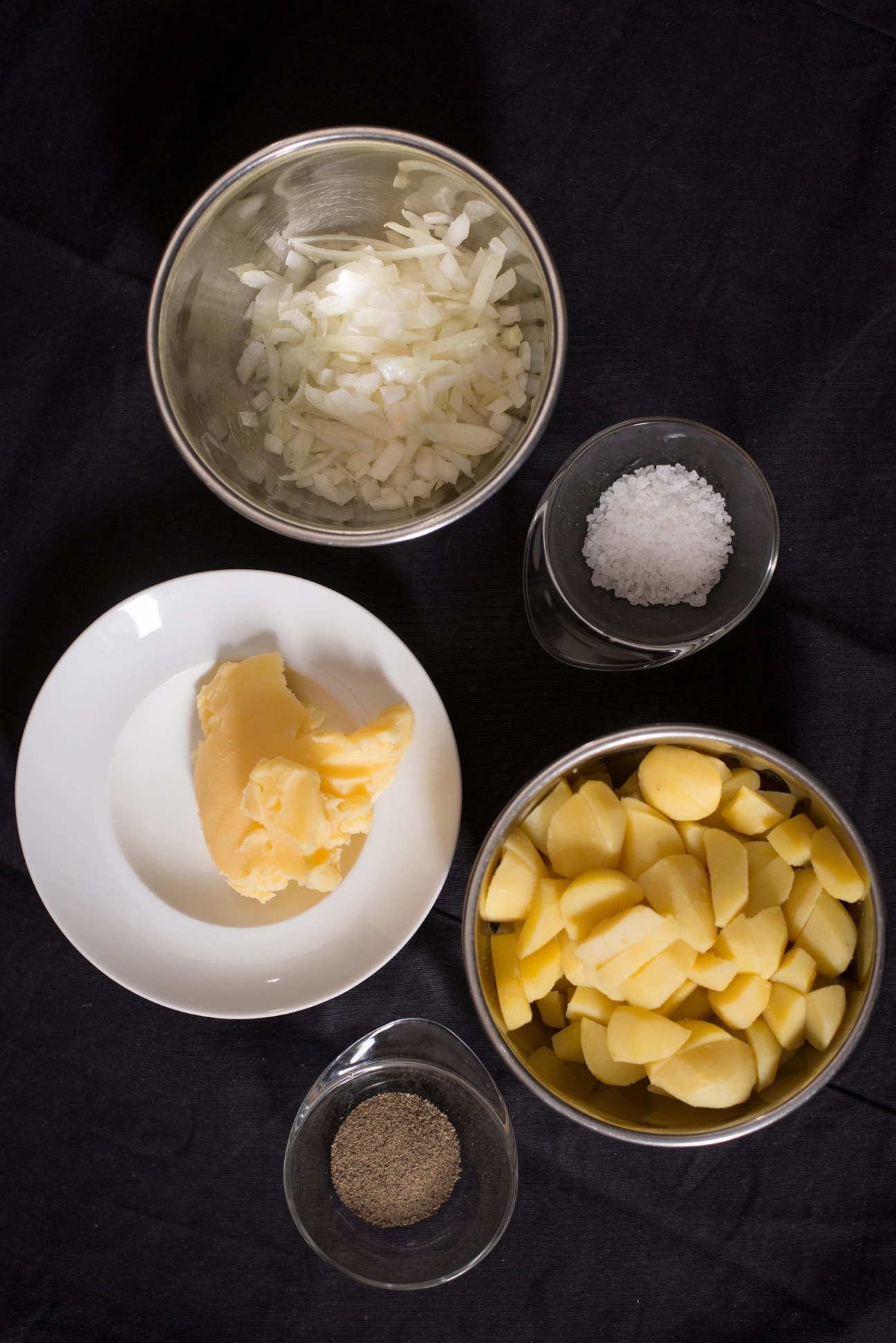 Ingredients for Bratkartoffeln fried potatoes including diced onions, butter, potatoes, salt and pepper in bowls.