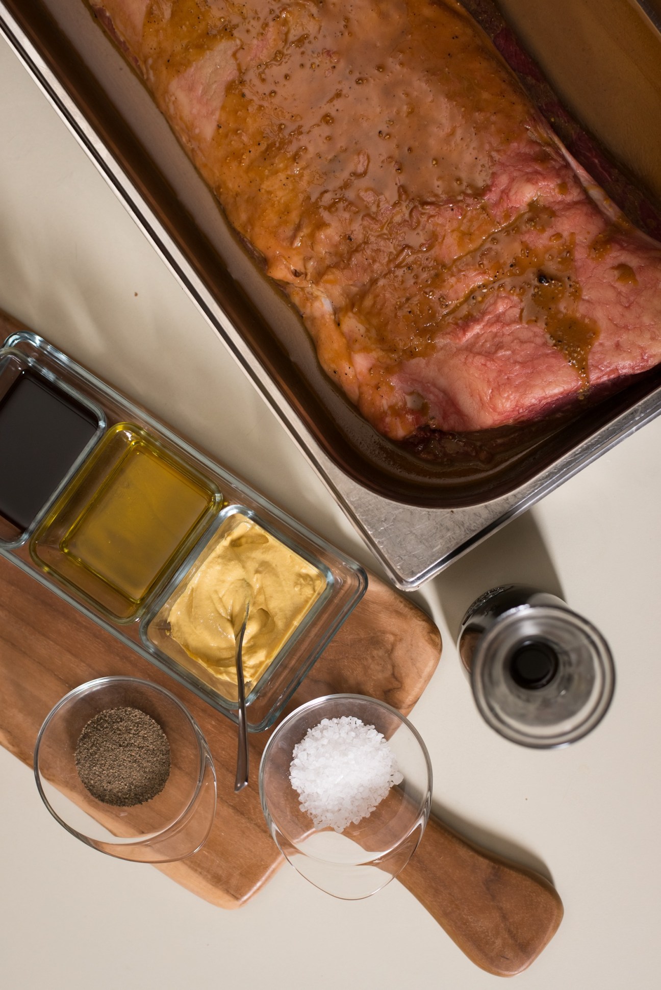 Rare roast beef with marinade ingredients including olive oil, mustard, salt and pepper arranged on wooden board.
