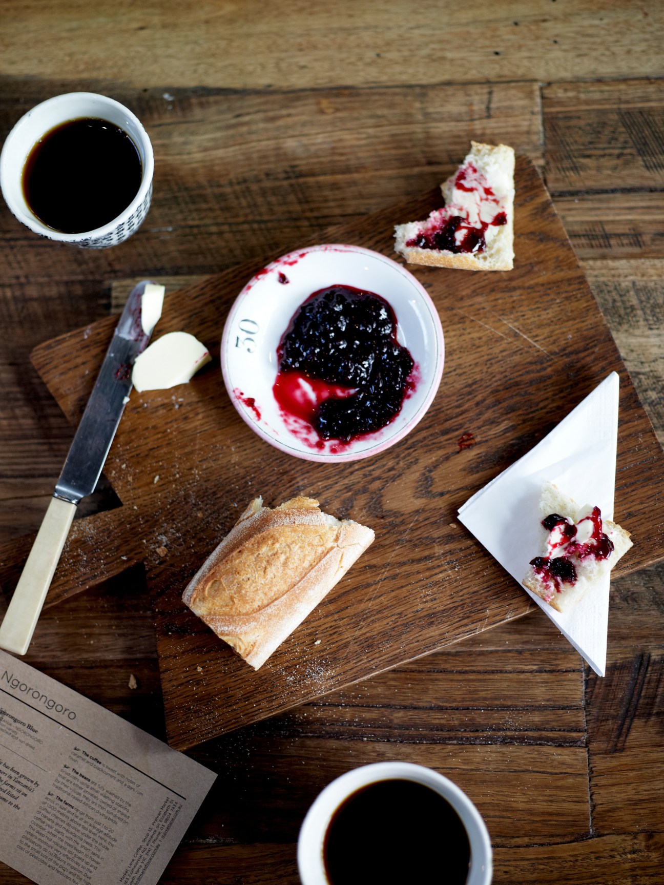 Overhead view of Market Lane Coffee's offerings: two black coffees, bread and jam on wooden plates, and berry-topped pastries on a wooden table.