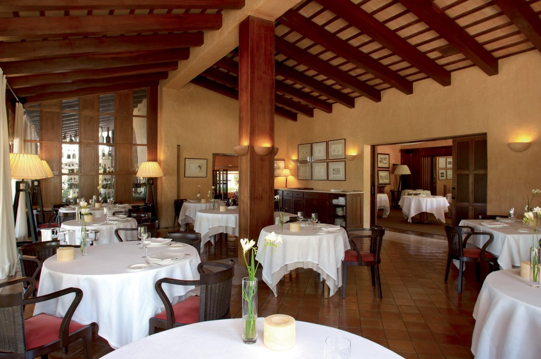 Elegant fine dining room at Mas de Torrent with white tablecloths, wooden beams, and framed artwork on walls.
