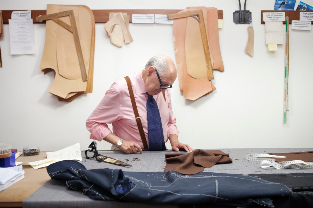 Elderly tailor Antonio Liverano working at his cutting table surrounded by fabric patterns and tailoring tools.