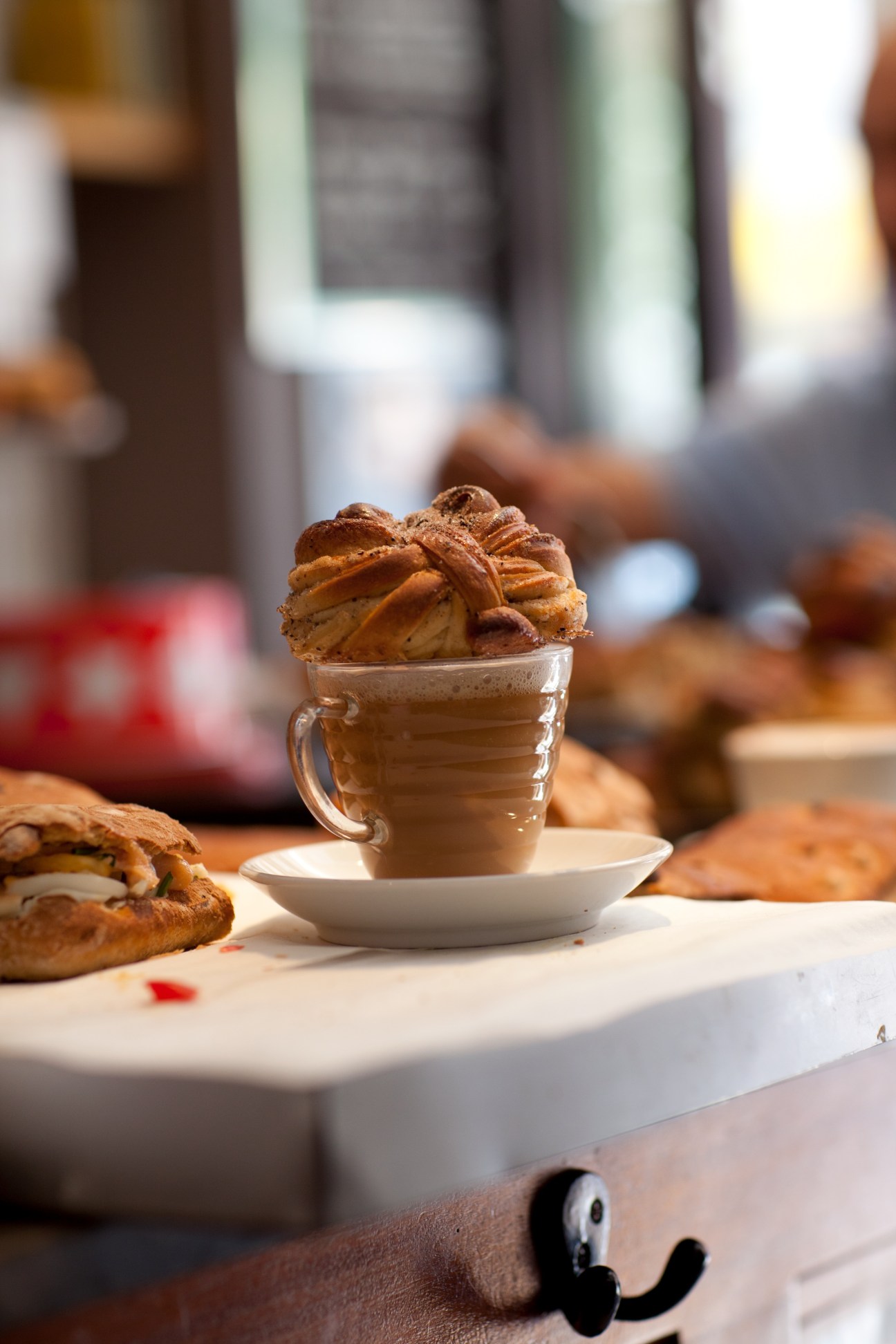Cappuccino with latte art topped with a croissant, surrounded by pastries on a white plate.