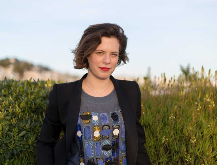 Alice Cabaret, founder of The Street Society, poses outdoors in a black blazer among coastal vegetation.