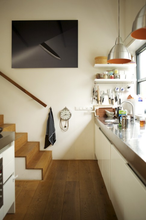 Modern kitchen with white cabinetry, wooden flooring, pendant lights, and minimalist wall decor.