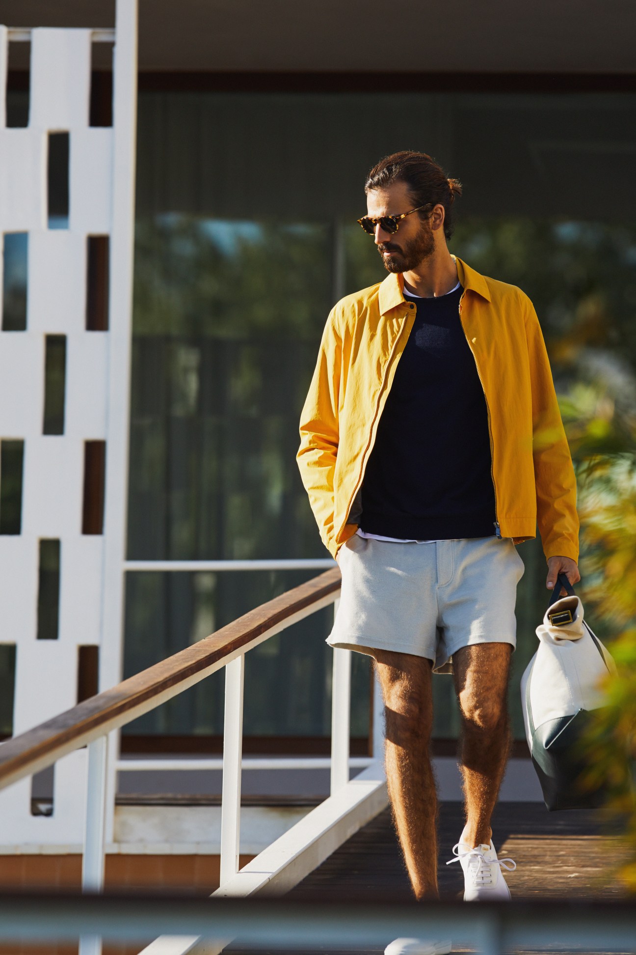 Man wearing yellow Z Zegna jacket, navy Kit and Ace t-shirt, and Hermès shorts on a modern balcony.