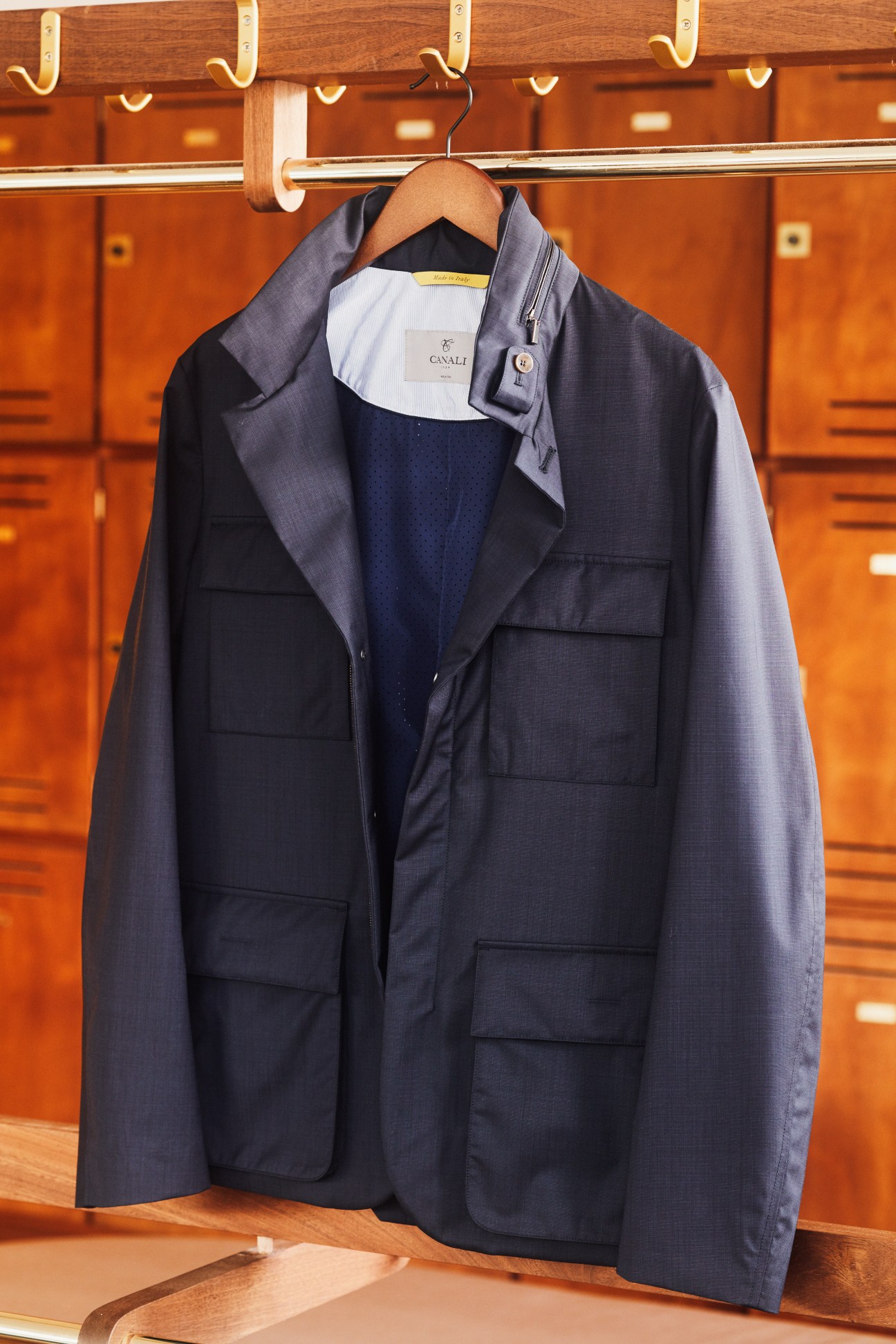Navy Canali jacket hanging on wooden hanger against orange locker backdrop.
