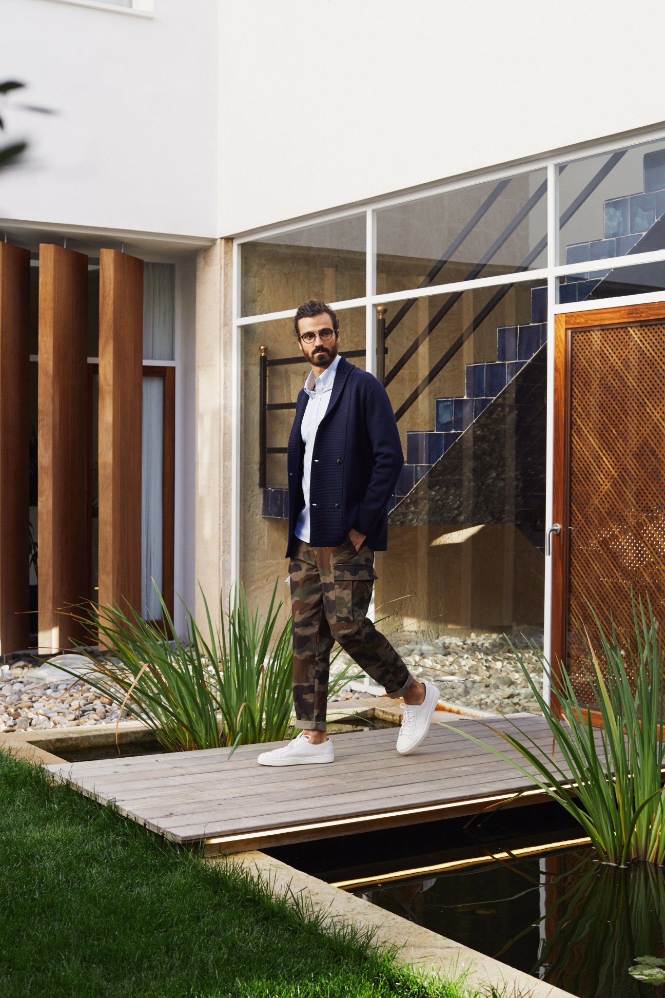 Man wearing Dunhill jacket and shirt with Moncler trousers and Santoni trainers standing on wooden deck at Palma Sport & Tennis Club.