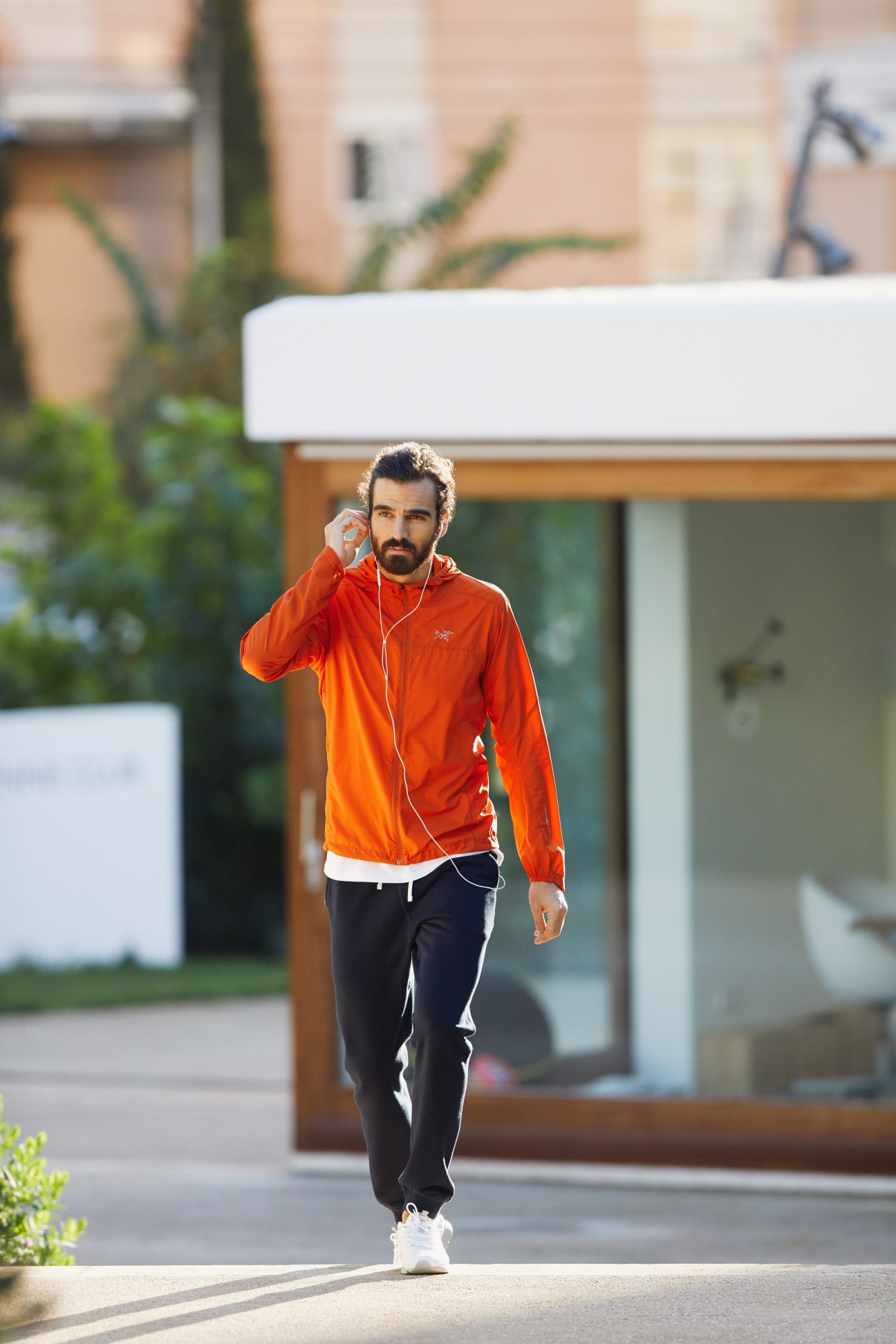 Man jogging in orange Arc'teryx hooded jacket, Kit and Ace t-shirt, Reigning Champ tracksuit bottoms and Asics trainers with Apple earphones.