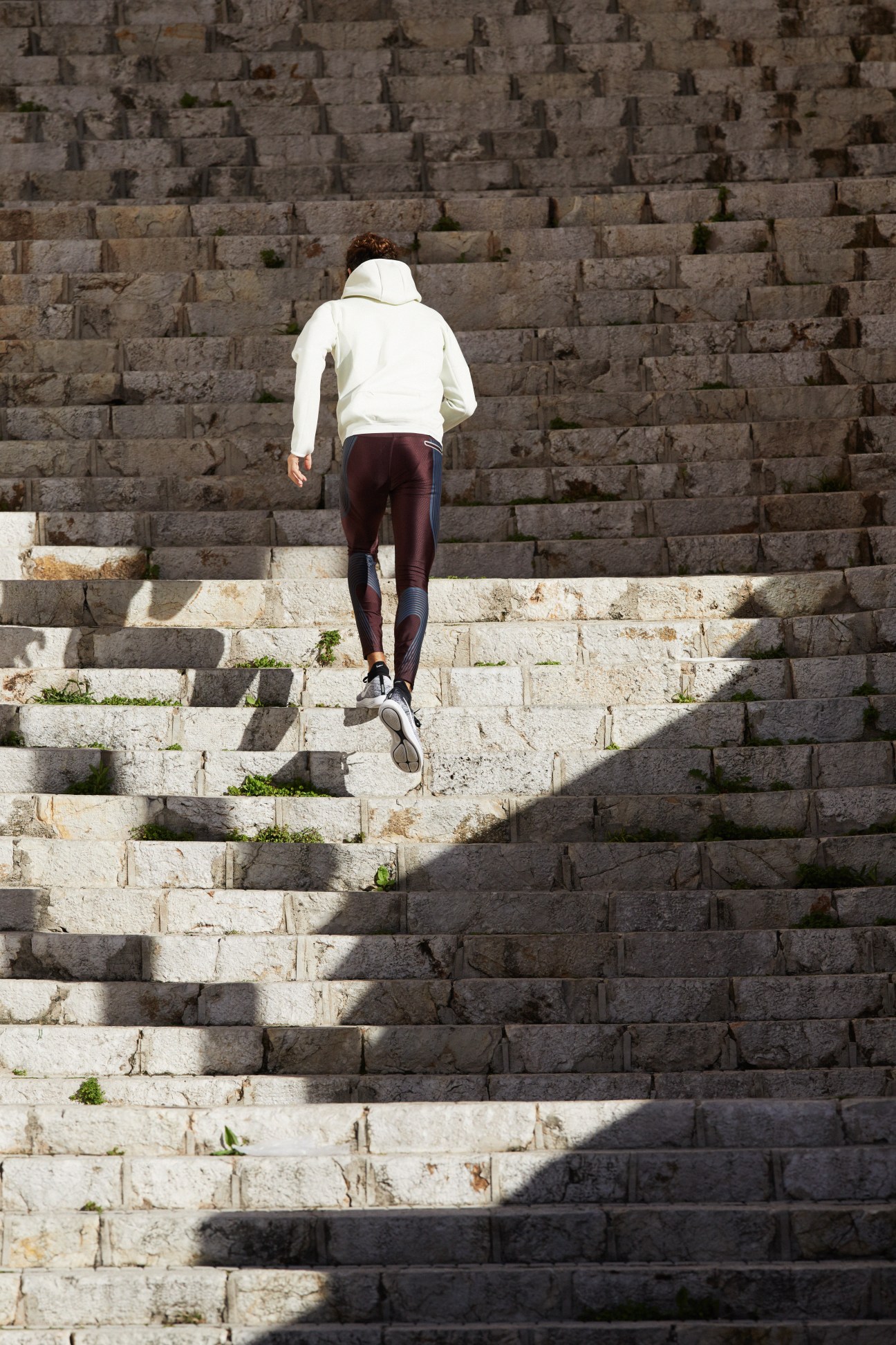 Runner in white hooded jacket and burgundy tights ascending stone steps.