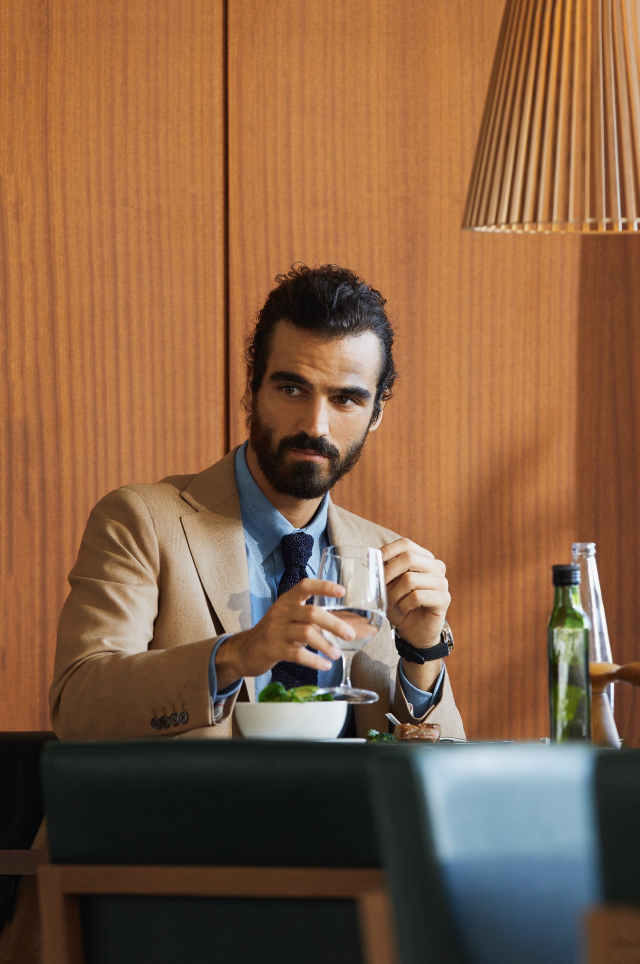 Man in Caruso jacket and shirt with Drake's tie holding a glass at a wooden-paneled bar.
