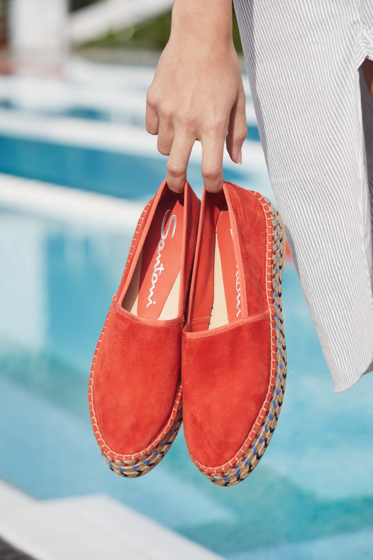 Hand holding red Havaianas flip-flops by a swimming pool.