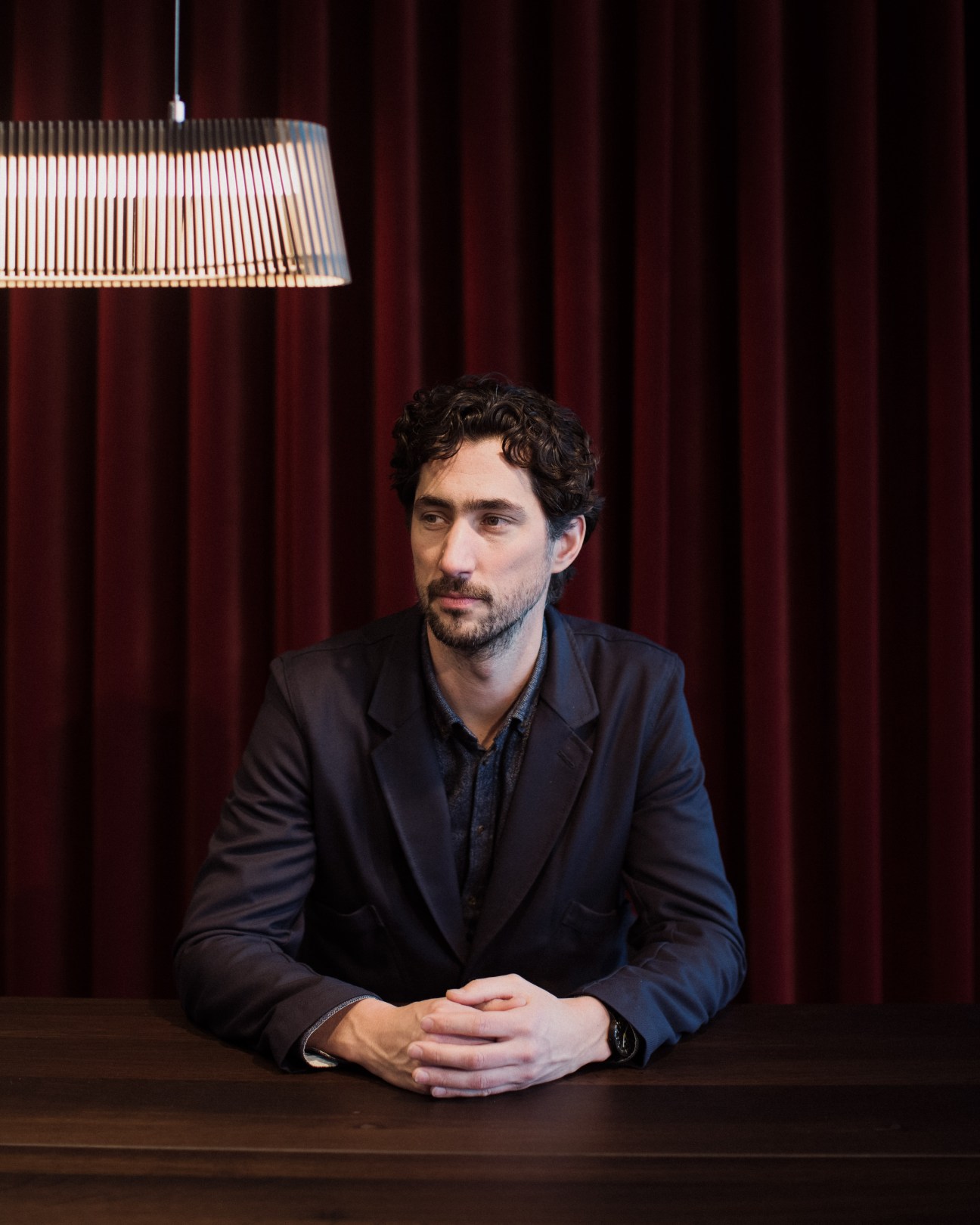 Jorre van Ast, director of Arco furniture company, seated at a table under a ribbed pendant lamp.