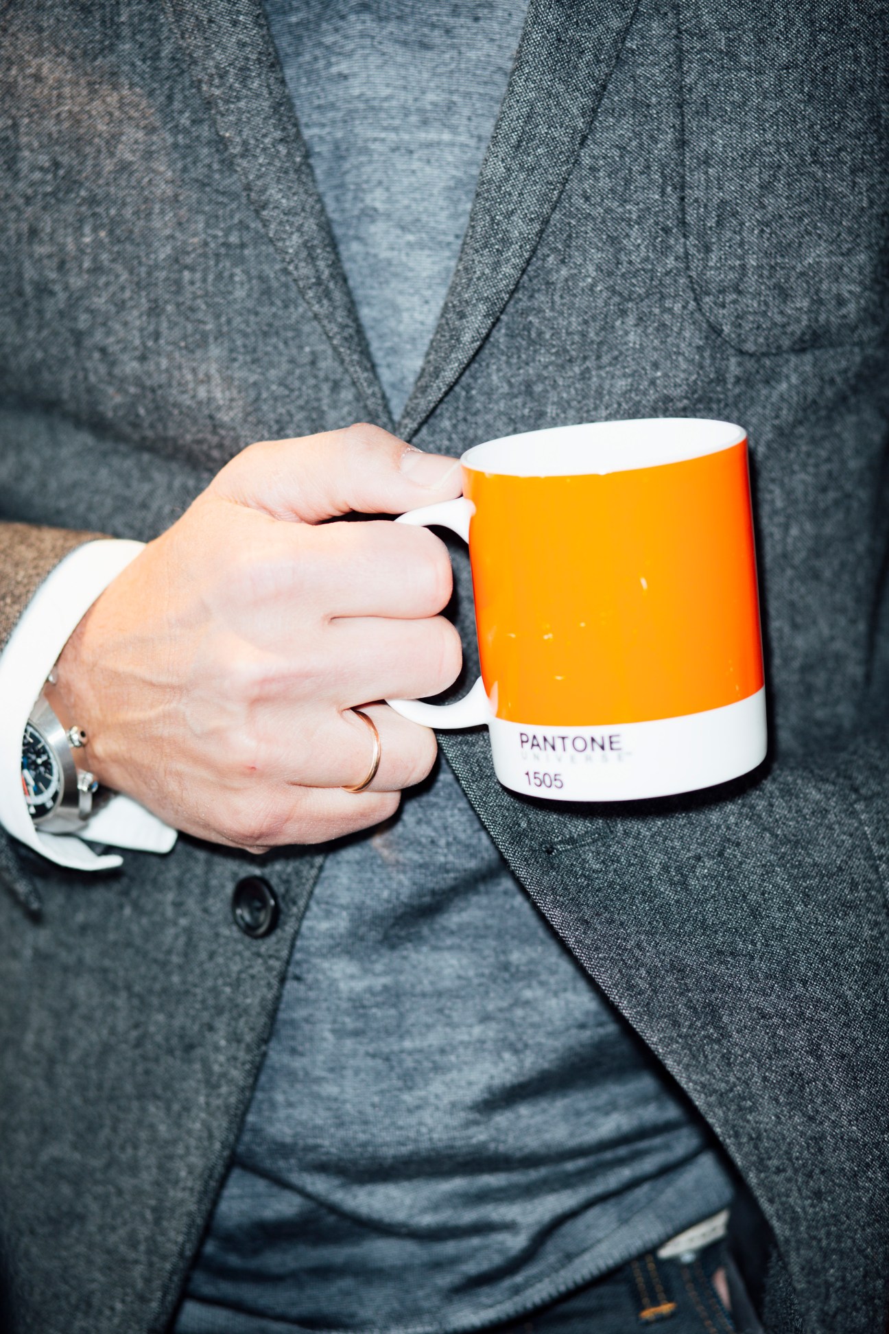 Man in grey suit holding an orange Pantone 1505 mug with white interior and base.