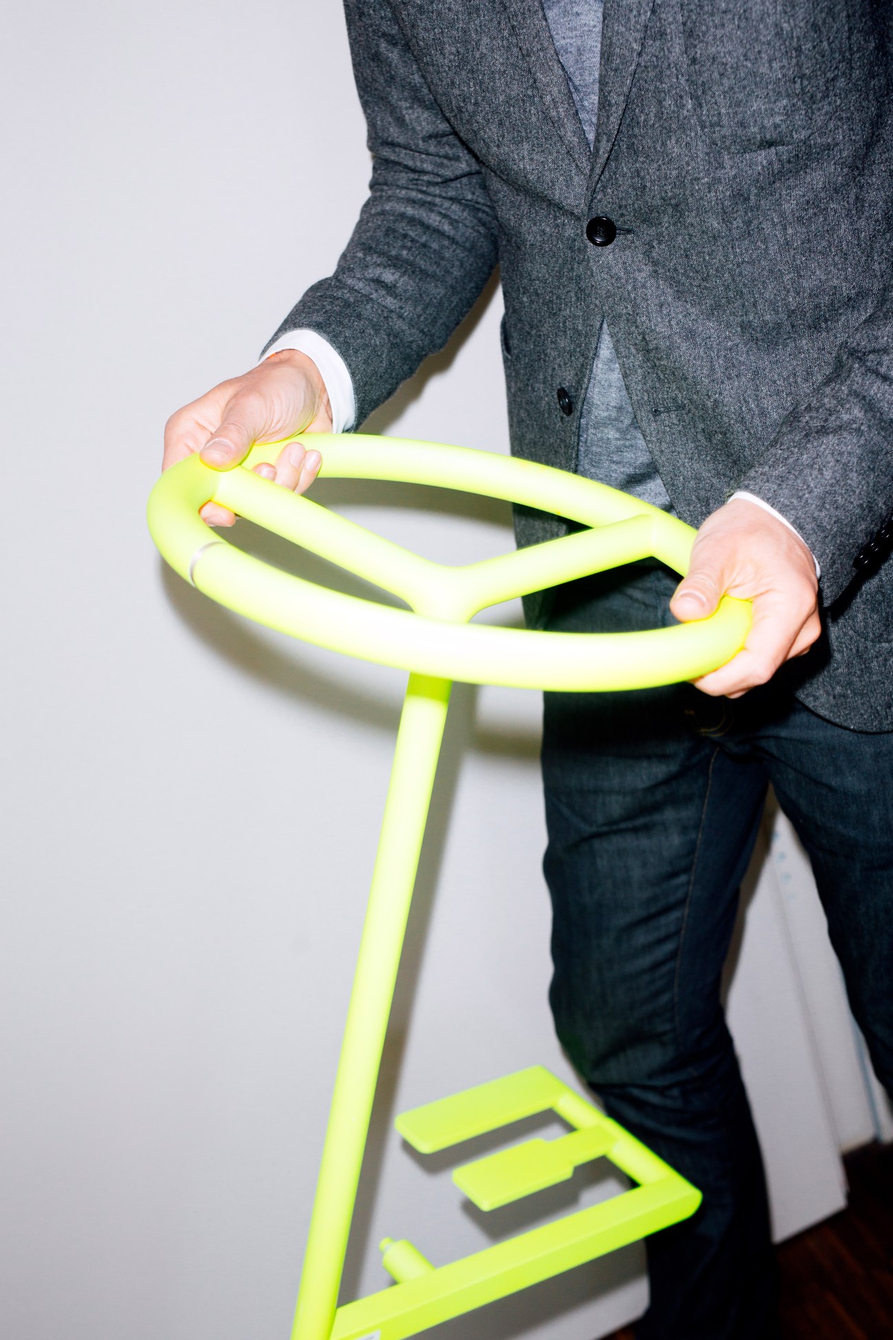 A person in a grey blazer holding a neon yellow steering wheel design