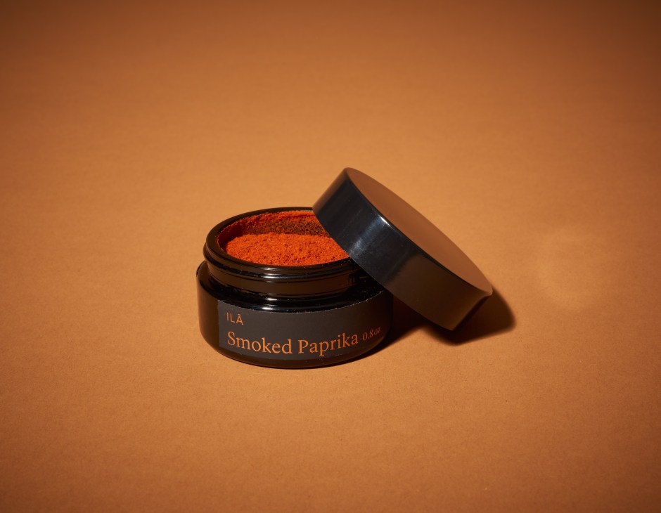 ILA Smoked Paprika in black jar with open lid showing red powder against tan background.