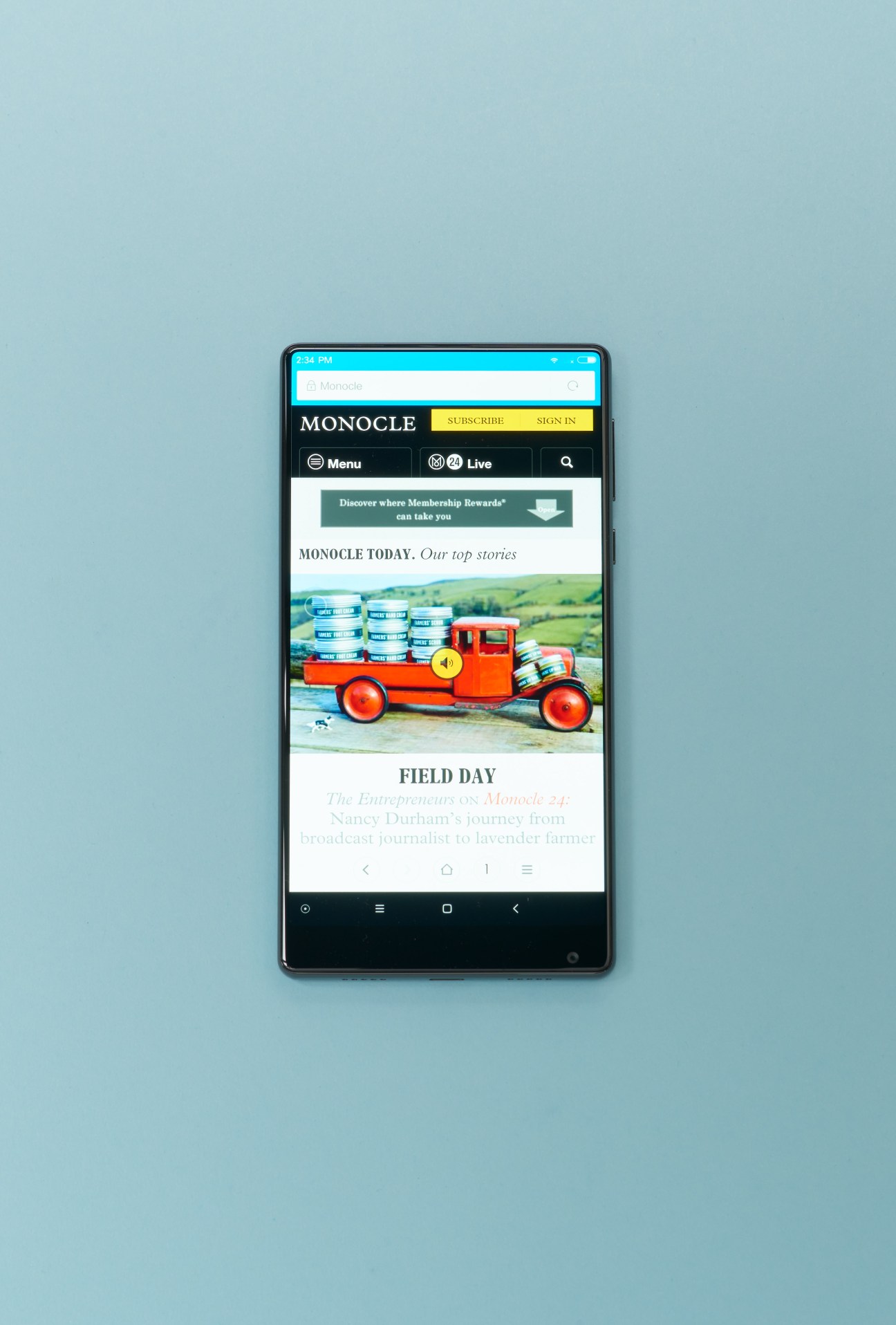 Smartphone displaying Monocle magazine website with an orange vintage truck loaded with blue containers.