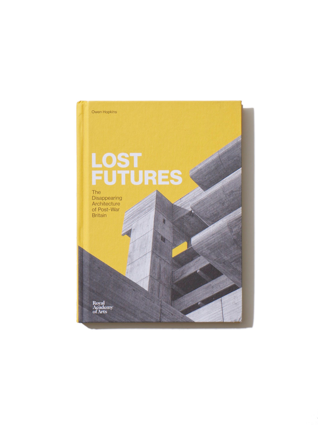 Yellow hardcover book 'Lost Futures: The Disappearing Architecture of Post-War Britain' by Owen Hopkins published by Royal Academy of Arts