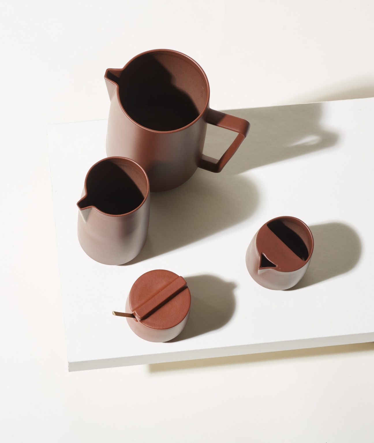 Yixing ceramic set in deep brown clay with jug, bowl, and smaller vessels arranged on white surface.